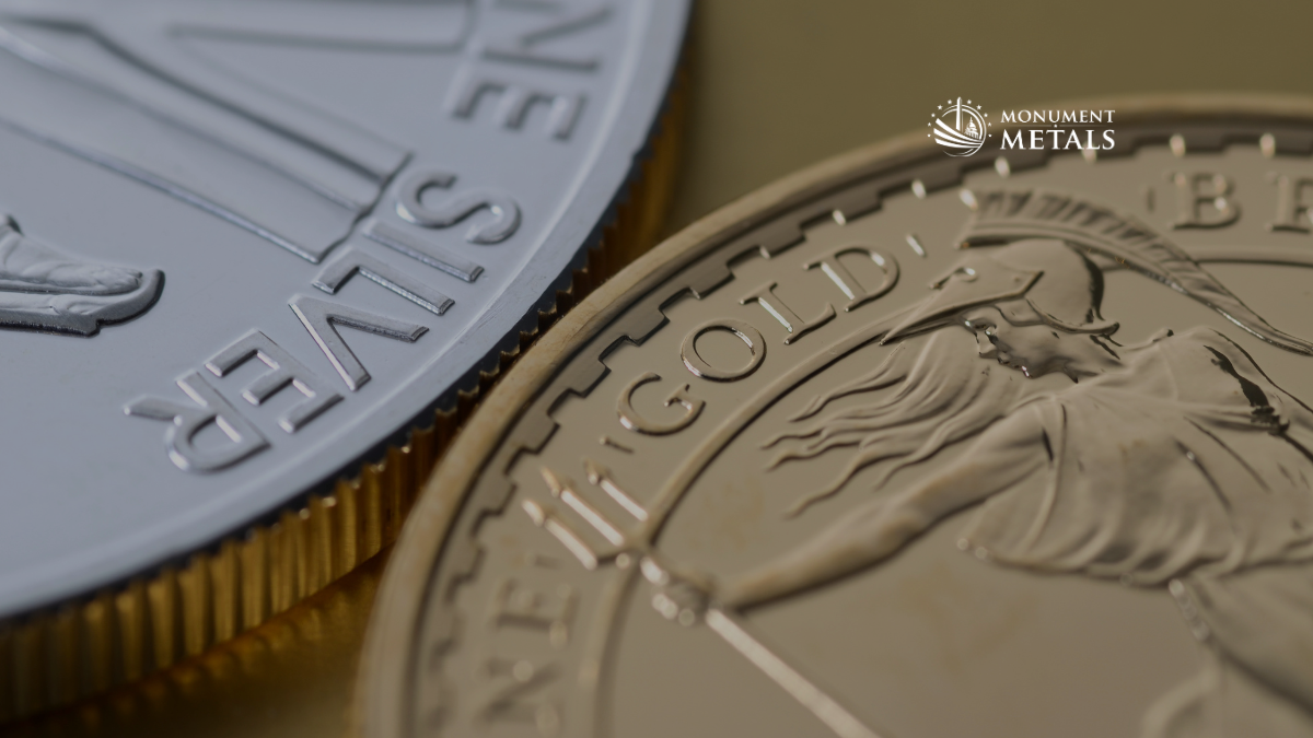 Close-up macro image of a silver coin and a gold coin side by side, highlighting detailed inscriptions and reeded edges, with the Monument Metals logo in the upper right, representing gold and silver bullion investment.