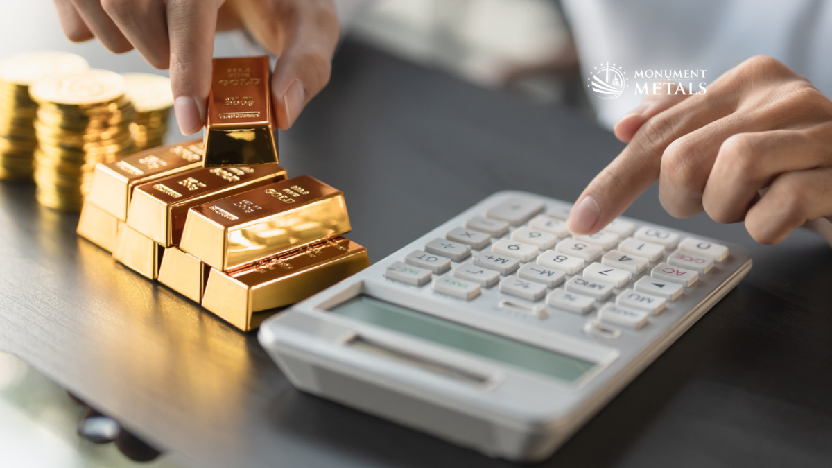Hands stacking gold bars next to a calculator, illustrating precious metals weight, value calculation, and the concept of troy ounces, with Monument Metals logo.